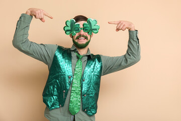 Young man in decorative glasses in shape of clover with green beard on beige background. St....