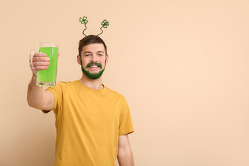 Young man in headband with green beard holding glass of beer on beige background. St. Patrick's Day...