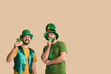 Young men in leprechaun hats with green beards holding clover on beige background. St. Patrick's...