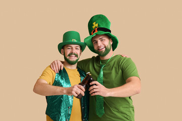 Happy young men in leprechaun hats with green beards holding bottles of beer on beige background....
