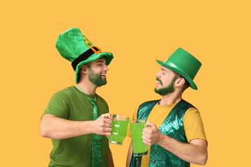 Young men in leprechaun hats with green beards holding glasses of beer on yellow background. St....