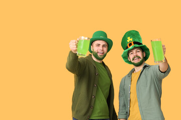 Young men in leprechaun hats with green beards holding glasses of beer on yellow background. St....