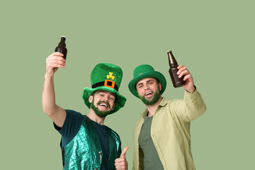 Happy young men in leprechaun hats with green beards holding bottles of beer on green background....
