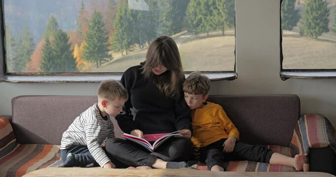 Mother on sofa reading a book to her kids in a mountain rustic chalet