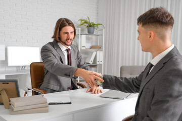 Young business men with bribe shaking hands at table in office. Corruption concept
