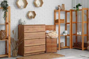 Interior of light laundry room with clothes basket, wooden dresser and shelving units