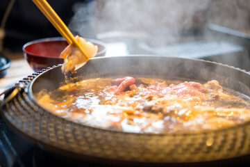 Holding sliced pork using chopsticks on hot pot with smoke for Japanese hot pot also known as Shabu Shabu or Sukiyaki is Japanese style.