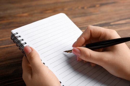 Female hand writing in blank notebook on wooden table, closeup