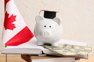Piggy bank with money and Canadian flag on books near light wall, closeup. Student loan concept