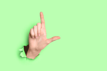 Hand of woman showing loser gesture visible through torn green paper