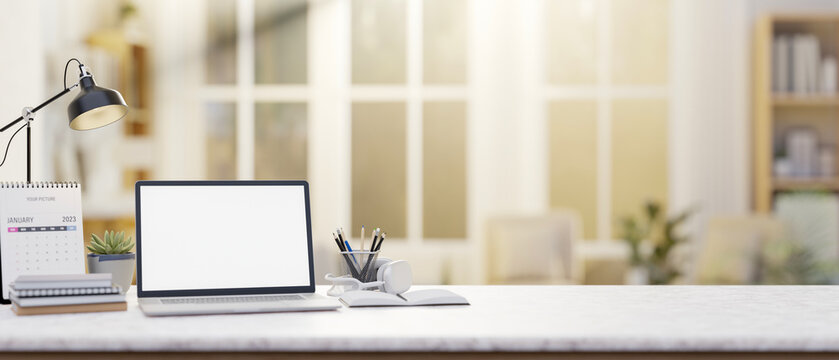 A laptop with a white screen placed on a white table with a blurry background of a living room.