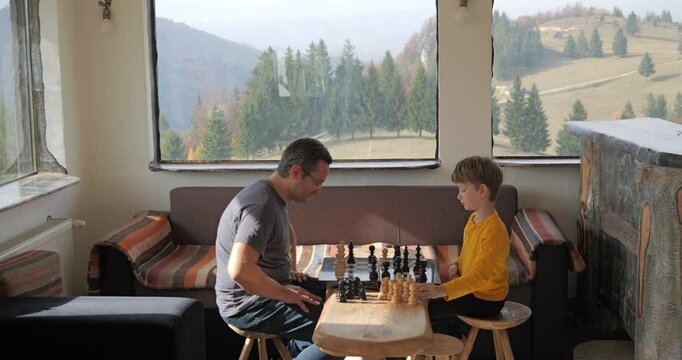 Man and kid play chess in a rustic mountain chalet