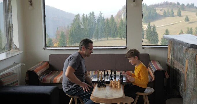Man and son play chess in a rustic mountain chalet