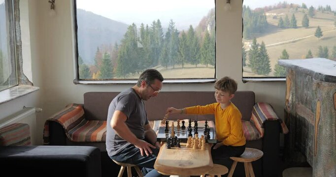 Father and son play chess in a rustic mountain chalet