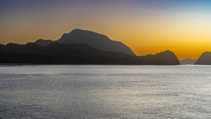 Naklejka premium Evening after sunset on a tropical island. The sky is gradiently highlighted in pink and orange. Picturesque silhouettes of mountains on the horizon. Ripples on the surface of a calm ocean.Philippines