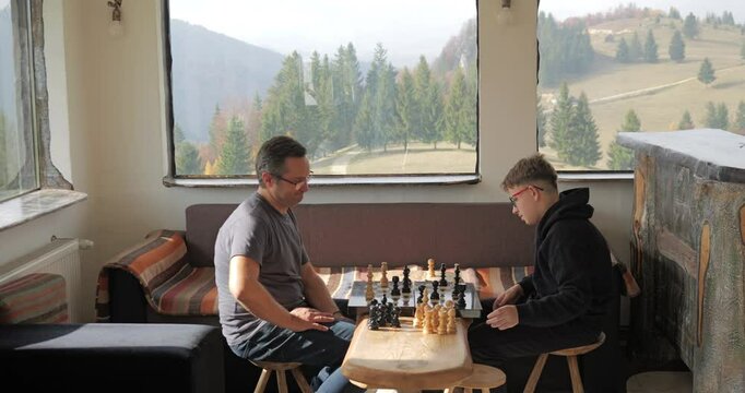 Man and his teen son playing chess in a rustic mountain cottage