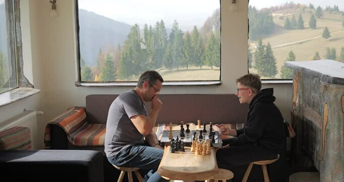 Teen checkmates his father at the chess game in the rustic mountain chalet