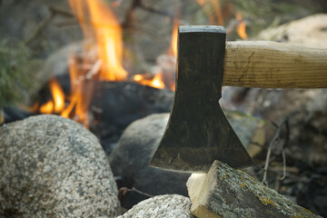 Axe splitting firewood near burning campfire outdoors