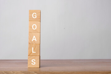 Goals word written vertically on wooden blocks on a wooden table with a light gray background....