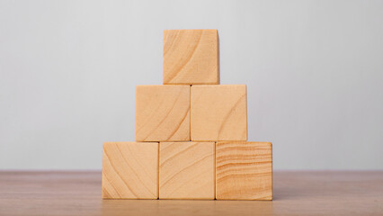 Wooden blocks stacked in a pyramid shape on a wooden table with a light gray background. Structure...