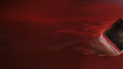 Red flow. Marbling stream. Liquid paint with smoky silky texture washes glass cube. Colored winding stream with blurred water abstract background.
