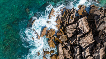 Granite rock formations with ocean waves splashing against them, surrounded by vibrant blue waters. Seychelles, La Digue.