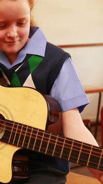 Cute pupil playing guitar in classroom