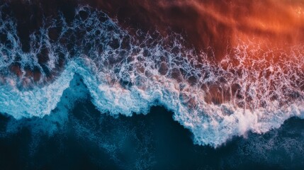 Aerial view of an ocean wave crashing on the shore at sunset