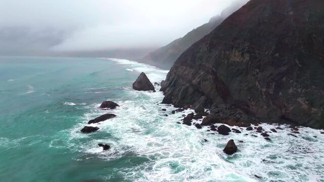 Rugged dramatic untouched coastline large surf waves USAL Beach campground aerial drone California PNW Lost Coast Trail cloud layer mist rain fog morning boulder rocks nature landscape circle right