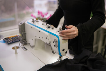 A seamstress diligently fixes a broken sewing machine, focused on her task amidst lively plants and bright daylight in the workshop.