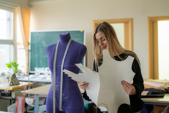 A designer skillfully adjusts a piece of fabric on a mannequin while surrounded by various sewing materials in a well-lit studio.