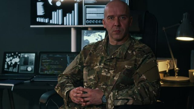Medium portrait of adult male Caucasian commander in military uniform confidently looking at camera while sitting at workplace in cybersecurity center