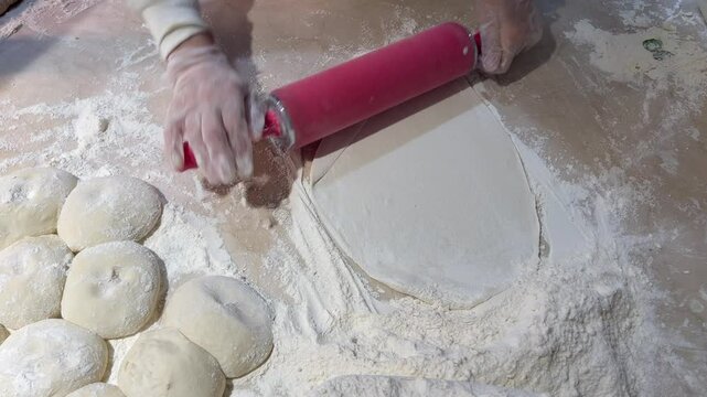Chef using a red bread roller pin to roll dough evenly