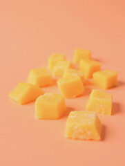 Bright yellow frozen mango cubes on light orange background