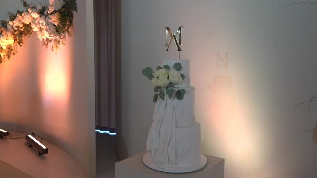 Three tiered white wedding cake adorned with floral decorations and a monogrammed topper