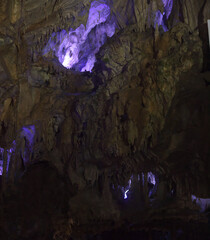 Dark cave wall with stalactites illuminated with flashlight