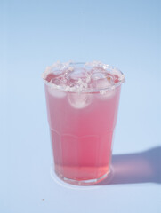 Refreshing pink lemonade in clear glass with ice on light blue background