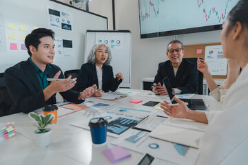 Fototapeta premium Asian businesspeople engaged in a meeting, discussing strategies while analyzing data and documents on the table in a modern office setting, fostering teamwork and collaboration