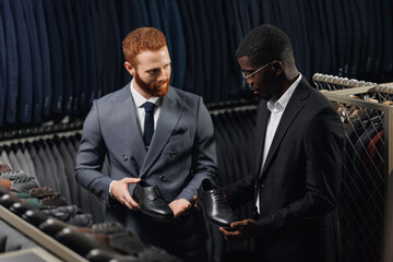 Seller of shoes in store helping of man in suit buy leather footwear