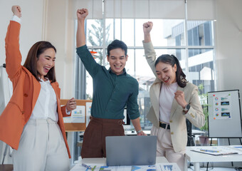 Euphoric businesspeople are raising arms and cheering while looking at laptop screen, celebrating...