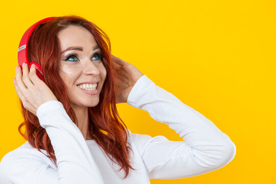 Closeup Portrait of smiling happy friendly woman in white casual shirt t-shirt wearing red wireless headphones isolated on yellow background studio portrait.