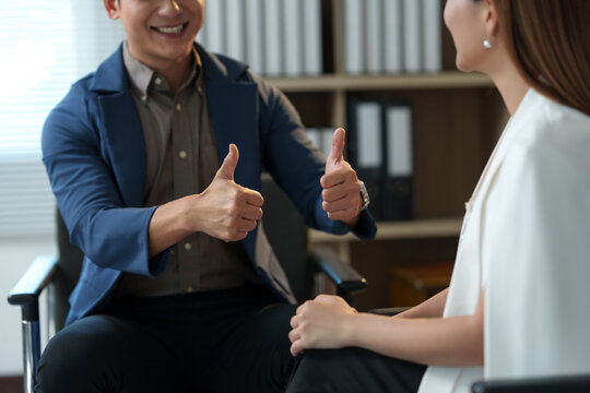Two smiling business people showing thumbs up gesture, expressing their satisfaction with successful agreement or project completion, positive feedback and approval concept