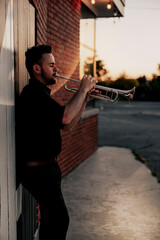 Trumpet player at sunset against brick wall