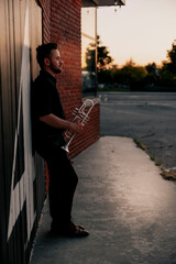 Relaxed trumpet player against brick wall at sunset