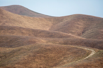 Rolling hills covered in brown grass with blue sky