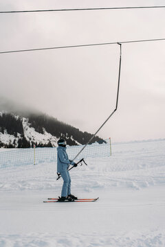 Young woman in blue ski suit climbs uphill on platter lift