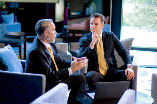 Young White businessman listening his senior partner explane project idea with concentrate at hotel lobby. Two generation business person have meeting.