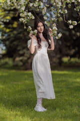 Naklejka premium Beautiful Girl with long hair poses near white blossoming apple trees