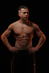 Fototapeta premium Adult male athlete bodybuilder posing on a orange light 