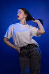 Young girl posing and moving in a black studio with colored light	